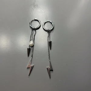 Silverörhängen med blixt och pärla - Snygga silverörhängen med hängande kedjor, en blixtformad detalj och en vit pärla. Perfekta för att ge en edgy touch till din stil.En pärla saknas så sänkt pris 