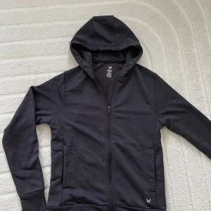 Svart huvtröja från SOC - Snygg svart huvtröja från SOC med dragkedja och långärmad design. Perfekt för en casual look med en stilren logga på framsidan. Tröjan har en bekväm passform och är tillverkad i ett mjukt material.