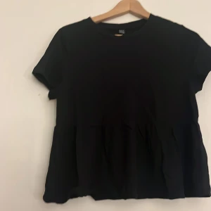 Svart topp med peplum -  Säljer en svart topp aldrig använd från Shein i storlek L. Toppen har korta ärmar och en rund halsringning. Perfekt för en avslappnad stil.
