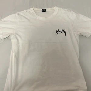 Stussy t-shirt - Säljer en vit t-shirt från Stüssy i storlek S. Den har en liten Stüssy-logga på bröstet och ett stort, coolt blommönster på baksidan. Perfekt för sommaren eller när du vill ha en avslappnad stil. T-shirten är i bomull och har korta ärmar. Den är i nyskick och redo för en ny ägare!