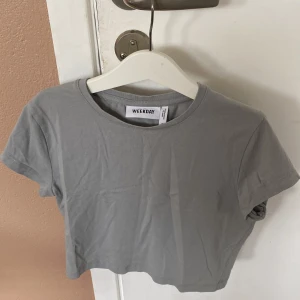 Grå croppad t-shirt från Weekday - Säljer en snygg grå croppad t-shirt från Weekday. Den är i storlek S och är perfekt för en casual look. T-shirten är kortärmad och tillverkad i ett mjukt bomullsmaterial. Perfekt för sommaren eller som en basplagg i garderoben. köparen betalar för frakt 