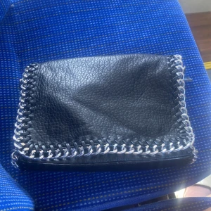 Svart skinnväska med kedjedetaljer - Säljer ( men byter helst mot en mindre design) en snygg svart skinnväska med coola kedjedetaljer längs kanterna. Perfekt för både vardag och fest! Väskan är i bra skick och har en stilren design som passar till det mesta. Köp den nu eller ge ett bud! 🖤tveka inte om ni har några frågor skriv till mig direkt🖤