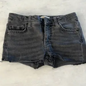 Säljer ett par svarta jeansshorts från Gina Tricot i storlek 134. De är i nyskick och har en snygg, sliten look med råa kanter. Perfekta för sommaren! De har en dragkedja och knapp framtill samt fem fickor. Superbekväma och stiliga för både vardag och fest.