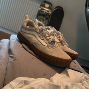 Vita sneakers från Vans - Säljer ett par vita Vans sneakers i storlek herr 38. Skorna är i mocka och har en snygg brun sula. De är i bra skick och har snörning. Perfekta för vår och sommar!
