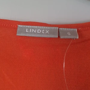 Orange blus från Lindex - Säljer en superfin orange blus från Lindex i storlek S. Blusen har korta ärmar och ett vackert broderat mönster över hela tyget. Den har en v-ringad hals och är perfekt för både vardag och fest. Materialet känns lätt och luftigt, vilket gör den idealisk för vår och sommar.