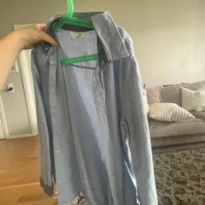 Ljusblå linneskjorta - Säljer en ljusblå skjorta i linne. Skjortan har långa ärmar och knappar framtill. Perfekt för en avslappnad men ändå stilren look. Passar bra till både vardag och fest.