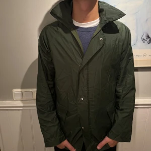 Grön regnjacka med justerbar huva - Säljer en grön regnjacka/vindjacka i bra skick