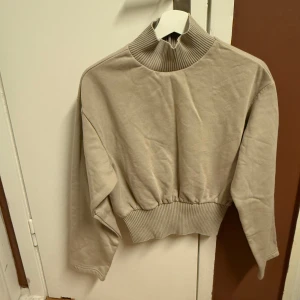 Beige tröja från Gina Tricot - Säljer en superfin beige tröja från Gina Tricot i storlek S. Den har en hög ribbad krage och långa ärmar, perfekt för höst och vinter. Materialet känns mjukt och skönt, och den har en ribbad kant vid midjan för en snygg passform.   