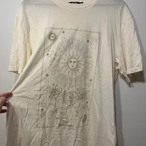 Vit t-shirt med soltryck - Säljer en vit t-shirt från BikBok med ett coolt tryck av en sol och blommor. Texten 'Soul Searching' finns längst ner på trycket. Perfekt för en avslappnad stil och passar till alla tillfällen. T-shirten är i bra skick och har en normal passform. Passar också S. Knappt använd 