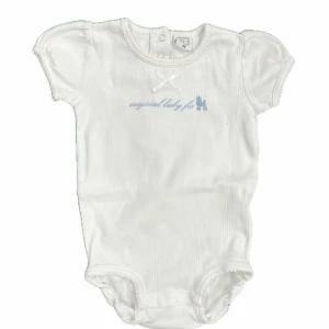 Vit babybody -  Vit babybody med korta puffärmar och en liten rosett framtill. Den har ett tryck i ljusblått med texten 'original baby fit'.  Knäppning i grenen för enkel på- och avklädning.