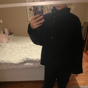 Svart kappa med knappar - Säljer en stilren mörkblå kappa med stora knappar framtill. Den har en lös passform och långa ärmar, perfekt för höst och vinter. Jackan är i mycket bra skick och passar både till vardags och fest. Ett måste i garderoben för den som gillar klassisk stil!