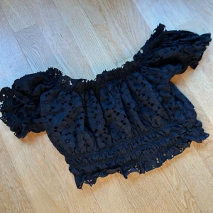 Svart blus från Gina Tricot - Säljer en superfin svart blus från Gina Tricot i storlek S. Den är kortärmad och har ett vackert broderat mönster med volangdetaljer. Går att ha Off shoulder eller som vanligt! Ryggen har öppna hål & i fram har den extra lager tyg! Inrelappen är bortklippt!🖤