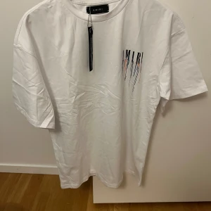 Vit t-shirt från Amiri - Säljer en snygg vit t-shirt från Amiri i nytt skick. Den har ett coolt tryck med färgglada detaljer både fram och bak. Perfekt för en avslappnad stil eller att klä upp med en jacka. Storleken är normal och materialet känns mjukt och skönt. Loose S