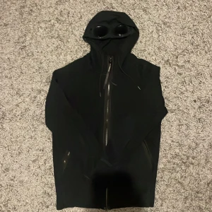 Svart CP company zip hoodie - Säljer en svart hoodie från C.P. Company med inbyggda glasögon i huvan. Den har en dragkedja framtill och är i mycket bra skick.