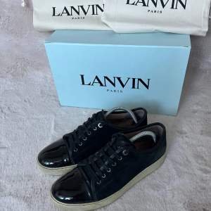 Säljer ett par snygga svarta sneakers från Lanvin i mycket bra skick. Skorna har en glansig finish och klassisk snörning. De kommer med originalkartong och dustbags. Perfekta för både vardag och fest! De ser lite fula ut i sulan fast är vitare i verklighet. Storlek 42