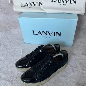 Lanvin - Säljer ett par snygga svarta sneakers från Lanvin i mycket bra skick. Skorna har en glansig finish och klassisk snörning. De kommer med originalkartong och dustbags. Perfekta för både vardag och fest! De ser lite fula ut i sulan fast är vitare i verklighet. Storlek 42