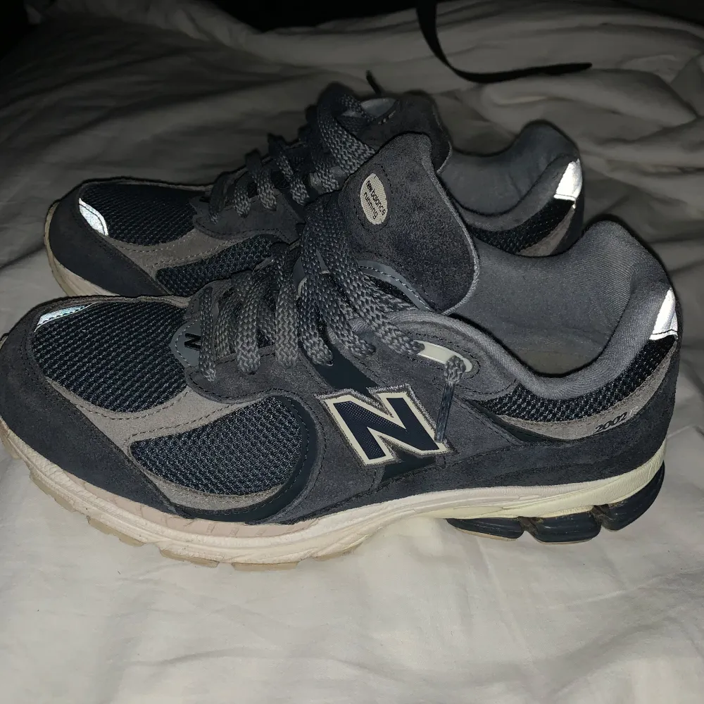 Säljer ett par New Balance sneakers i grått och svart. De har en snygg och sportig design med snörning och är i bra skick. Perfekta för både vardag och träning. Storlek 41.5 EU. 2002r. Skor.