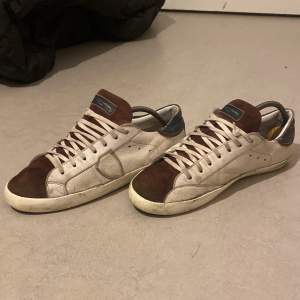 Säljer ett par Philippe Model sneakers i beige och brun mocka med skinn. De har en snygg vintage-look med snörning och en bekväm passform. Perfekta för både vardag och festliga tillfällen. Lite slitna men fortfarande i bra skick.