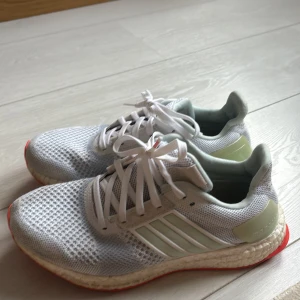 Vita Adidas Ultraboost sneakers - Säljer ett par vita Adidas Ultraboost sneakers i mycket bra skick. De har en snygg och stilren design med vit mesh och grå detaljer. Perfekta för både träning och vardag. Skorna har en bekväm passform och Boost-sula för extra komfort.