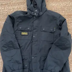 Säljer en svart Barbour jacka i mycket bra skick. Den är vattentät och andas, perfekt för höst och vinter. Jackan har en huva och flera praktiska fickor med knappar. Klassisk och stilren design som funkar till det mesta. Passar perfekt för kyliga dagar! Storlek XL i ungdomsstorlek! 