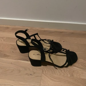 Svarta sandaler med klack - Snygga svarta sandaler med klack och elegant snörning. Perfekta för sommarens fester eller en kväll ute. De har en bekväm passform och en stilren design som passar till många olika outfits.