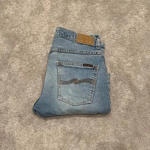 Nudie Grim Tim Jeans - Säljer ett par ljusblå jeans från Nudie i storlek 30/30. Modellen är Grim Tim. De har en klassisk femficksdesign och är i extremt bra skick utan defekter. Perfekta för både vardag och fest! Fraktar på köparens bekostnad samma dag som beställning. 