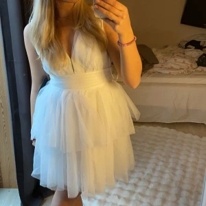 Vit kortklänning med volang - Säljer en superfin vit kortklänning med volangdetaljer. Den har en v-ringad design och är perfekt för sommarens fester. Klänningen är ärmlös och har en luftig passform som ger en romantisk känsla. Perfekt för både student och midsommar!