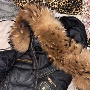 Svart dunjacka med päls från Rockandblue - Säljer en snygg svart jacka från Rockandblue i storlek 36. Pälsen är i väldigt, väldigt fint skick. Jackan och håller dig varm trots att du bär en tunn tröja under! Använd en vinter, trots det jätte fint skick. Några sömmar i mönstret på utsidan som gått upp lite men absolut ingenting som syns, varken när man har på sig den eller om man bara tittar på den. Nypris 3200.