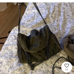 Grå axelväska med kedjedetaljer - Snygg grå axelväska, liknande Stella mcartney,  mellan modellen och rymmer mycket, dragkedjan på utsidan är sönder men i övrigt är väskan super bra skick 