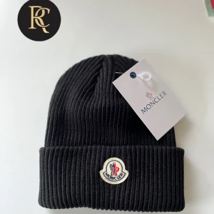 Svart ribbad mössa från Moncler - Snygg svart ribbad mössa från Moncler i nytt skick. Den är perfekt för vintern med sin stilrena design och varma material. Mössan har Monclers ikoniska logga framtill och är i en klassisk svart färg som passar till allt. Perfekt för både höst och vinter