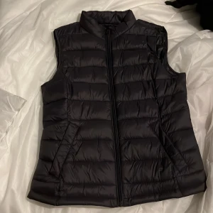 Svart dunväst från Vila - Säljer en svart dunväst från Vila i storlek 34. Västen har en dragkedja framtill och är perfekt för kyliga dagar. Den är quiltad och ger en snygg och stilren look. Passar bra till både vardag och fest. 🖤