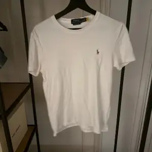 Säljer en klassisk vit t-shirt från Polo Ralph Lauren i custom slim fit. Den har en liten broderad logga på bröstet och är i mycket bra skick. Perfekt för både vardag och fest! 👕✨