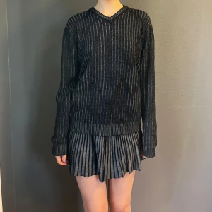 Svartgrå stickad batistini tröja - Snygg svart stickad från batistini med ett diskret randigt mönster. Den har långa ärmar och en v-ringad hals. 2XL men passar bra oversized. 50% ull / 50% akryl