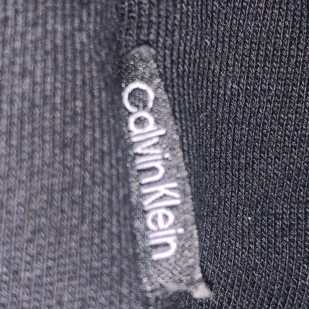 Säljer en stilren svart hoodie från Calvin Klein. Den har en klassisk passform med justerbar huva och det ikoniska Calvin Klein-logotypen tryckt på framsidan. Perfekt för en avslappnad look eller att mysa i hemma. Passar till alla säsonger!. Neuletakit & Villapaidat.