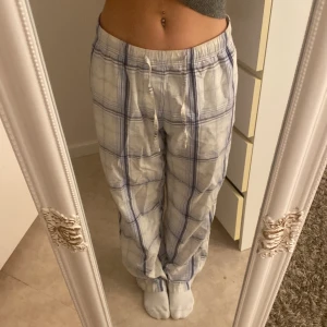 Mysbyxa - Säljer ett par superbekväma byxor i vitt med blått rutmönster. De har en avslappnad passform och snörning i midjan för extra komfort. Perfekta för mysiga hemmakvällar eller en avslappnad dag ute. 🛋️💙