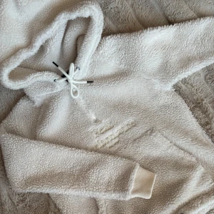 Vit fleece hoodie - Mysig vit fleece hoodie perfekt för kalla dagar. Den har en stor ficka fram och justerbar dragsko i huvan. Supermjuk och varm, idealisk för både hemmamys och utomhusaktiviteter. Passar perfekt till höst och vinter!