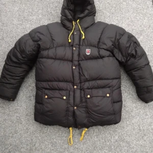 Fjällräven down expedition jacka - Ännu en fin vinter jacka på lagret med små disfekter då det är ett smått hål och ett lagat hål som man ser på bild 4,5 men inget som fångar ett öga. Den är herr S men passar även tjejer med L-XL