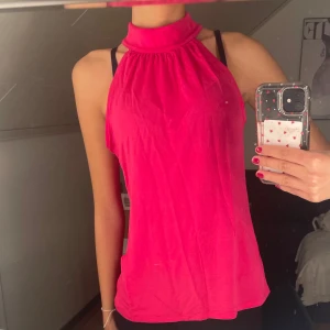 Rosa ärmlös topp - Säljer en snygg rosa ärmlös topp med hög hals. Perfekt för sommardagar eller en utekväll. Toppen har en lös passform och är gjord i ett mjukt material som känns skönt mot huden. Passar bra till både jeans och kjol!🩷🩷