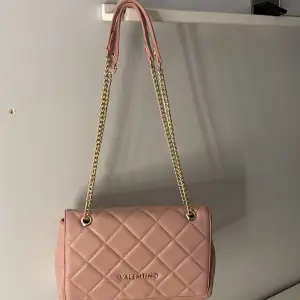 Säljer en superfin rosa axelväska från Valentino i quiltat mönster. Väskan har en elegant guldkedja som axelrem och är perfekt för både vardag och fest. Den är helt oanvänd och ger en lyxig touch till vilken outfit som helst. Perfekt för dig som älskar stil och kvalitet! Vill sälja då jag inte uppskattat färgen såsom jag trodde, köpt på zalando för ca 1200kr. Priset går att diskutera. Högsta bud får.