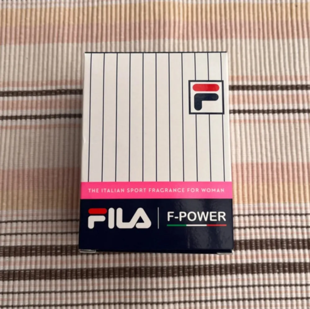 Säljer en sportig och fräsch parfym för kvinnor från FILA, F-Power. Flaskan är stilren och fyrkantig med en röd kork och en stor blå logotyp på framsidan. Perfekt för den aktiva och moderna kvinnan som vill ha en doft som matchar hennes livsstil. Kommer i en snygg förpackning med vita och rosa detaljer.              Fila | F-power The italian sport fragrance for woman Oanvänd 90ml. Parfym.