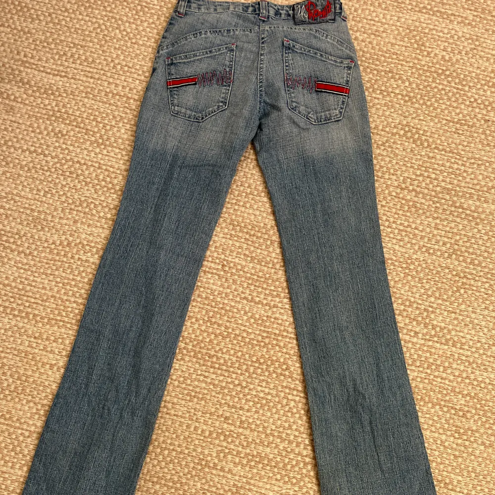 Säljer ett par snygga blå jeans i storlek 36. De har coola röda och svarta detaljer på bakfickorna och en dragkedja fram. Perfekta för en casual look med en twist! Innerbenslängd: 87cm, midjemått:34cm. Jeans & Byxor.