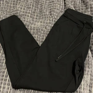 Svarta mjukisbyxor med snörning - Säljer ett par svarta mjukisbyxor i mycket bra skick. De har en bekväm passform med snörning i midjan för justerbarhet. Perfekta för en avslappnad dag hemma eller en snabb tur till affären. Materialet är mjukt och skönt, vilket gör dem till ett måste i garderoben.