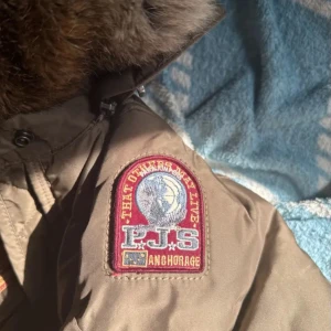 Brun dunjacka från Parajumpers - Säljer en brun dunjacka från Parajumpers i mycket bra skick. Jackan har en fluffig pälsfodrad huva och dragkedja framtill. Perfekt för kalla vinterdagar. Den är både snygg och funktionell med flera praktiska fickor och detaljer.