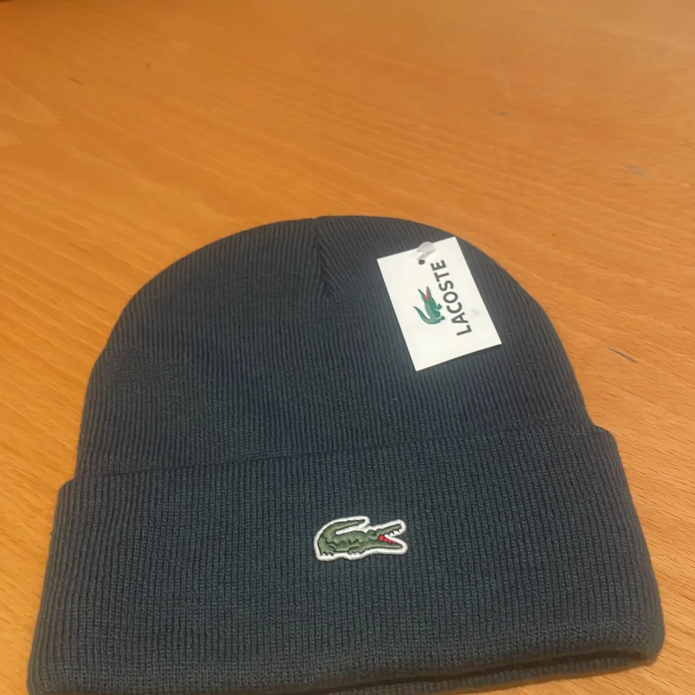 Snygg och stilren mörkblå stickad mössa från Lacoste. Perfekt för kyliga dagar med sin mjuka och bekväma passform. Den har Lacostes ikoniska krokodillogga broderad framtill. Ett måste för vintern!. Accessoarer.