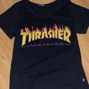 Säljer en svart Thrasher t-shirt i bomull med det ikoniska flammande logotyptrycket i gult och rött. Perfekt för en casual look eller skateparken. T-shirten är kortärmad och i mycket bra skick. Passar perfekt till jeans eller shorts!