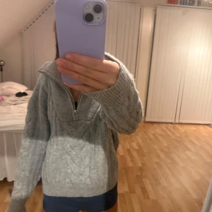 Grå stickad tröja från Stay - Mysig grå stickad tröja från Stay i storlek XS. Den har en dragkedja framtill och ett snyggt flätmönster. Perfekt för kyliga höst- och vinterdagar. Tröjan har långa ärmar och en hög krage men kan vikas ner. Superfin att matcha med jeans eller leggings! 