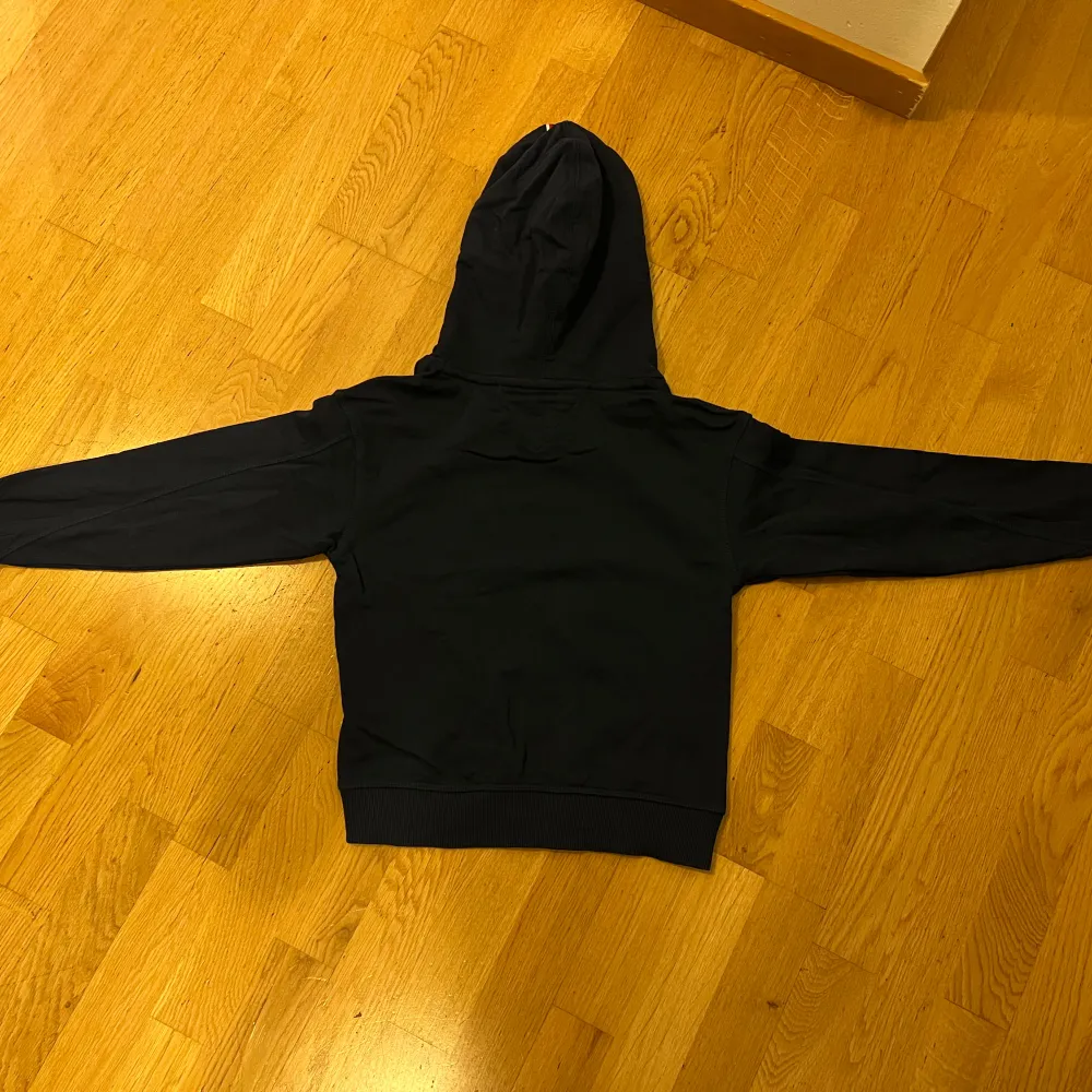 Säljer en snygg marinblå hoodie från Tommy Hilfiger i storlek 140 (barnstorlek). Den har en klassisk design med loggan tryckt på framsidan och en bekväm huva. Perfekt för både vardag och chill. Passar bra till jeans eller joggers! Nypris 695kr. Använd ett fåtal gånger. Inga fläckar eller skador. Pris går att diskuteras! . Neuletakit & Villapaidat.