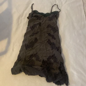 Mörkgrå spetsklänning - Säljer en elegant mörkgrå klänning med spetsdetaljer. Den har smala axelband och en vacker spetskant vid halsringningen. Perfekt för en festlig kväll eller en utekväll. Klänningen är i bra skick och har en normal passform.