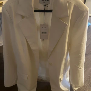 Vit kavaj från NA-KD - Säljer en stilren vit kavaj från NA-KD i storlek EU 36. Kavajen har en klassisk design med långa ärmar och en knapp framtill. Perfekt för både vardag och fest! 🕊️