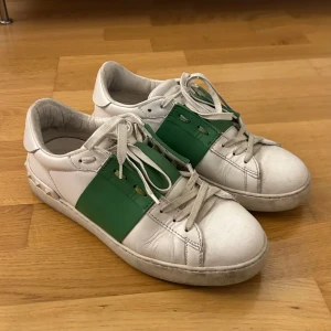 Valentino sneakers med gröna detaljer - Valentino-sneakers i vitt skinn med gröna detaljer. Använt skick men inga defekter bortsett från en nit på ena skon där spetsen delvis ”trubbats av”. Storlek 40, något stora i storleken. Ursprungligen köpta på Vestiaire Collective så självklart äkta, kan skicka bild på orderbekräftelsen. Lågt pris då inga tillbehör följer med pga jag fick själv inga sådana vid originalköpet 💚